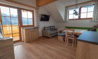 A cozy living room with wooden flooring and modern furniture. Large windows offer a view of the mountains.