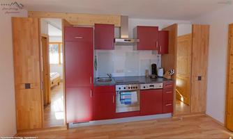 A modern kitchen with red cabinets and a cooking island. The room has a bright wood floor and large windows that provide plenty of light.