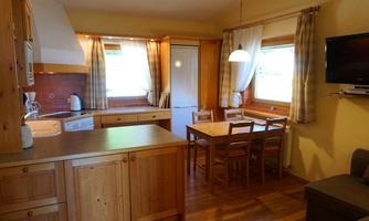 A cozy kitchen with wooden furniture and a dining table. Windows let in a lot of light and give the room an inviting atmosphere.