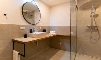 A modern bathroom with a large shower and a wooden washbasin. The round mirror and bright lighting create an inviting atmosphere.