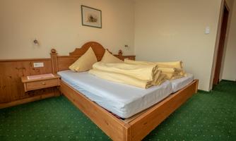 A simple bedroom with a large bed and yellow bedcovers. The floor is covered with green carpet and there is a nightstand next to the bed.