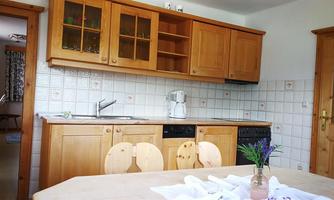 A modern wooden kitchen with a friendly atmosphere. There is a dishwasher, a coffee machine, and a table with flowers.