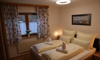 A cozy bedroom with a double bed and bright pillows. The windows are decorated with beautiful curtains, and a soft light creates an inviting atmosphere.