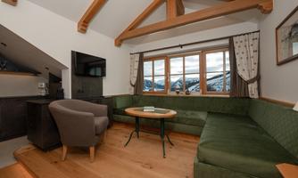 A cozy living space with a green couch, a round table, and a television. Large windows offer a view of the mountains and provide bright light.