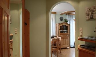 A cozy interior with green walls and wooden furniture. The view shows a dining area through a beautiful arch.