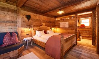 A cozy wooden room with a double bed and a seating area. The walls are made of light wood, creating an inviting atmosphere.