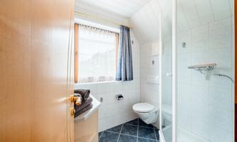 A modern bathroom with a shower, toilet, and bright tiles. A window front provides natural light.