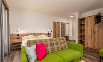 A modern room with a green sofa and a large bed. The walls are light and the wooden furniture creates a cozy atmosphere.