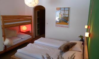A cozy bedroom with a double bed and a bunk bed. The walls are painted green, and there is appealing lighting as well as a decorative poster.