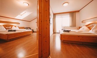 A spacious room with two beds, wooden materials, and a large window. The floor is made of wood and the room is bright and inviting.