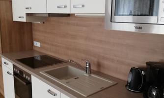 A modern kitchen with white cabinets and wooden accents. It is equipped with a stove, a sink, and appliances such as a microwave and a coffee machine.