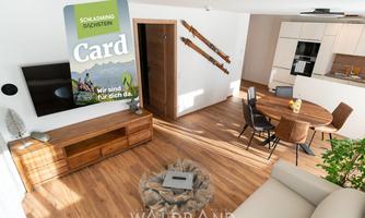 A modern living room with a bright, inviting ambiance. In the room, there is a cozy sofa, a wooden table, and an informative map about activities in Schladming.