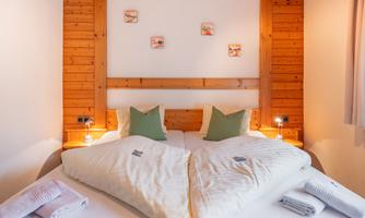 A cozy bedroom with two beds and wooden paneling. On the beds, there are pillows and blankets designed in soft colors.