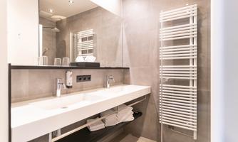 A modern bathroom with a long sink and elegant fixtures. On the wall, there is a towel radiator.
