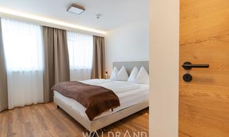 A modern bedroom with a double bed and a warm color selection. Bright windows and simple curtains create an inviting atmosphere.