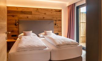 A modern bedroom with two single beds and wooden panels on the wall. Large windows let in plenty of daylight.