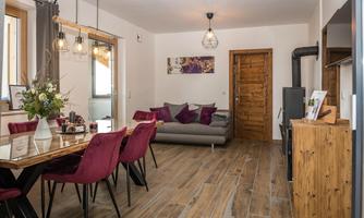 A modern living room with a cozy sofa and a dining table. The decor is stylish and inviting, featuring warm wooden tones.