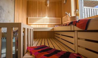 A modern sauna with wooden paneling and benches. Ceiling lamps and a towel create a relaxing atmosphere.