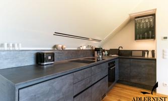 A modern kitchen unit with gray surfaces and wooden flooring. The equipment includes a refrigerator, a sink, and several kitchen appliances.