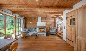 A cozy living space with wooden paneling and a fireplace. Large windows offer a view of the nature outside.