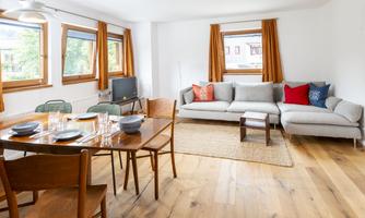 A modern living room with a cozy sofa and a dining table. Large windows let in plenty of light and create a bright atmosphere.
