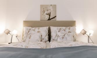 A cozy bedroom with a large bed and beautiful pillows. The walls are light, and there are decorative nightstands with lamps.