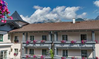 A picturesque building with balconies adorned with blooming plants. In the background, majestic mountains can be seen under a blue sky.
