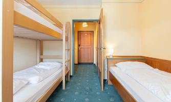 A simple bedroom with a bunk bed and a single bed. The room has a warm, inviting atmosphere and a door that leads to a hallway.