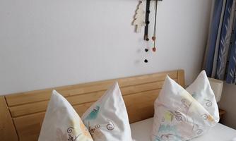 A comfortable bedroom with a wooden bed and decorative pillows. Creative elements hang on the wall, creating a cozy atmosphere.
