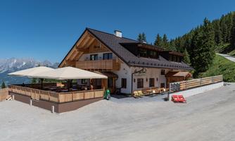 A cozy mountain house surrounded by green trees and mountains. The terrace is spaciously designed and invites you to linger.
