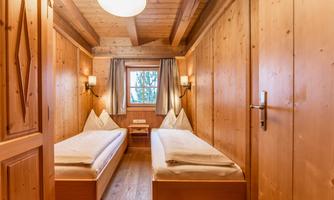 A cozy wooden bedroom with two single beds. Large windows let in plenty of light and create a relaxed atmosphere.