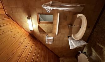 A small, cozy bathroom with wooden paneling. There is a sink, a toilet, and a mirror above the sink.