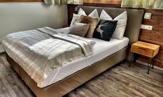 A cozy bedroom with a large bed and soft pillows. Next to the bed is a small wooden bedside table.
