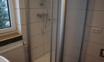 A modern shower with two glass walls in a bathroom. In the background, a window offers a view of snow-covered trees.