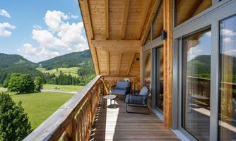 A quiet balcony with wood paneling and comfortable chairs. In the background, there are green hills and a blue sky with white clouds.
