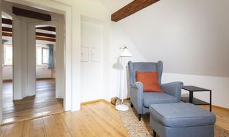 A cozy room with a blue seating area and a small table. The floor is made of wood and the walls are painted white.