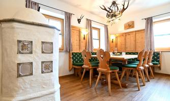 A cozy dining area with wooden furniture and green cushions. The walls are adorned with wood paneling and traditional decorations.