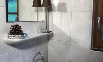 A modern bathroom with a small sink and a mirror. There is a decorative shelf with a pine cone and a lamp.