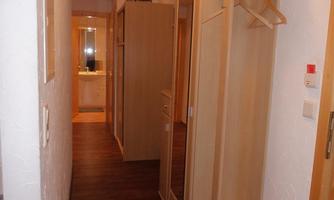 A narrow hallway with wooden furniture and a mirror. At the end of the hallway, a bathroom is visible.