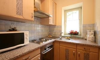 A bright kitchen with wooden cabinets and modern appliances. Flowers are by the window and the furnishings are functional.