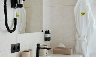 A modern bathroom with a sink, a towel rack, and a mirror. A bathrobe and a hairdryer hang on the wall.