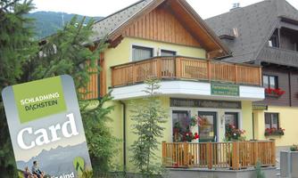 A charming house with wooden balconies and flowers. In the foreground, there is a map for the Schladming-Dachstein region.