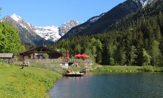 A picturesque mountain lake with a wooden house and red sun loungers. The surrounding mountains are snow-capped, and the nature is green and vibrant.