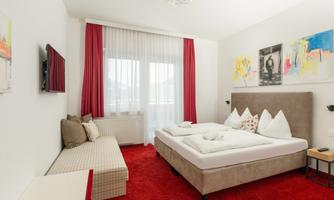 A modern room with a double bed and fresh décor. Red curtains and a soft carpet create a cozy atmosphere.