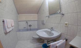 A modern bathroom with bright tiles and a wooden ceiling. There is a sink, a bathtub, and towels with a small bucket.