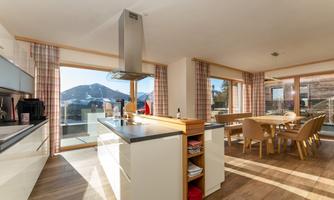 A modern kitchen with large windows and a view of the mountains. The dining area is bright and inviting with wooden chairs and a table.