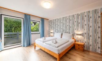 A bright bedroom with a double bed and two nightstands. Large windows let in plenty of daylight and provide a view of the outdoors.