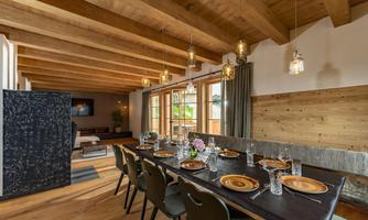 A bright dining area with a long table that is beautifully set. The wooden ceilings and large windows create a warm atmosphere.
