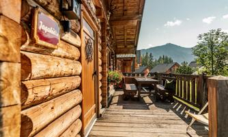 A cozy wooden terrace with a table and a view of the mountains. The sun is shining and the surroundings feel inviting.