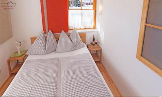 A cozy bedroom with a double bed and checked pillows. The room has large windows with plenty of daylight and a friendly, warm atmosphere.
